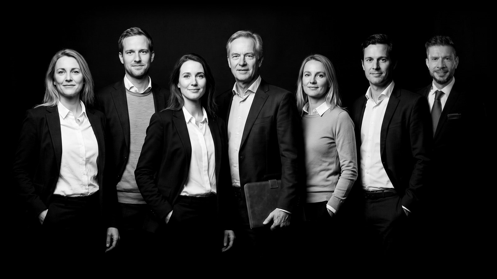 Gruppenbild Team Österreich: sieben Personen in Businesskleidung vor schwarzem Grund, Schwarz-Weiß